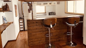 A kitchen with wooden paneling, a clock, and two bar stools. - Hakuba Ski Condos (Hakuba)