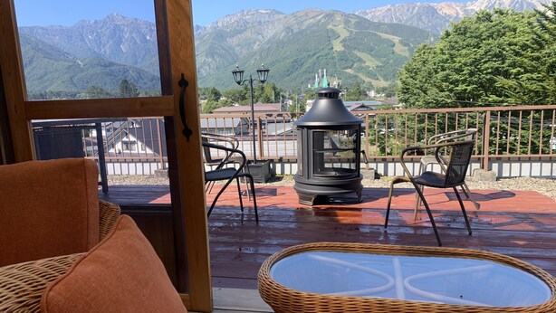 A wooden deck with wicker furniture, a glass table, and a black lantern. - Hakuba Ski Condos (Hakuba)