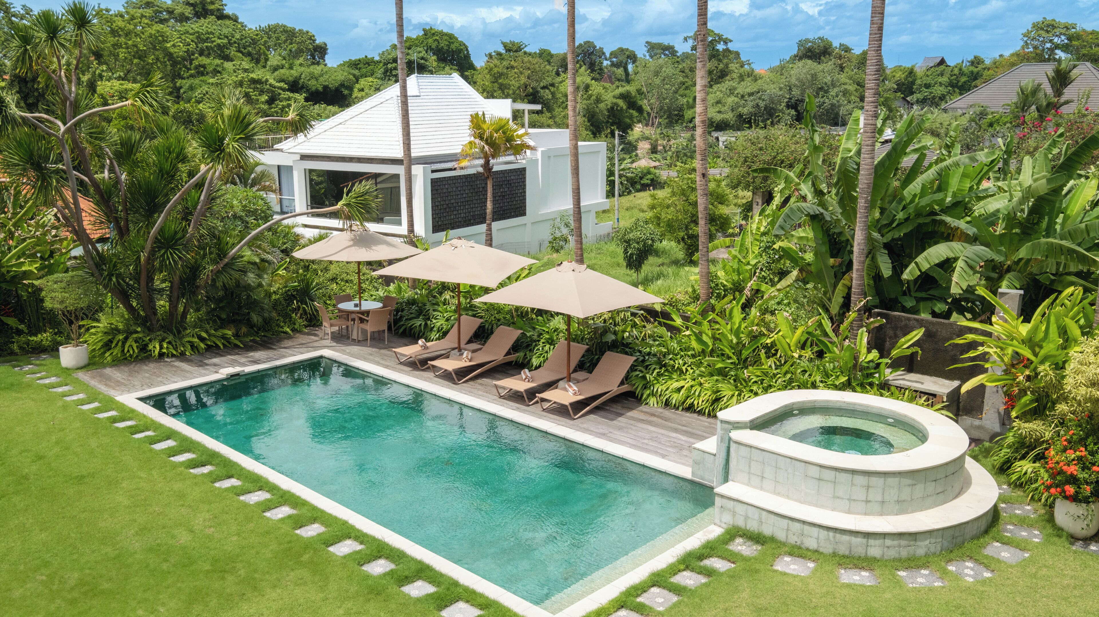 A swimming pool with lounge chairs and umbrellas, surrounded by lush greenery and a modern house.