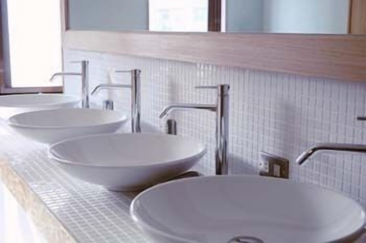 A bathroom with three white vessel sinks and a mirror above them.