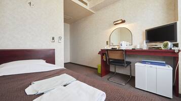 A hotel room with a bed, a desk with a computer, a television, and a small refrigerator.