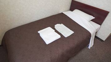 A single bed with a brown textured bedspread, two neatly folded white towels, and a wooden headboard.