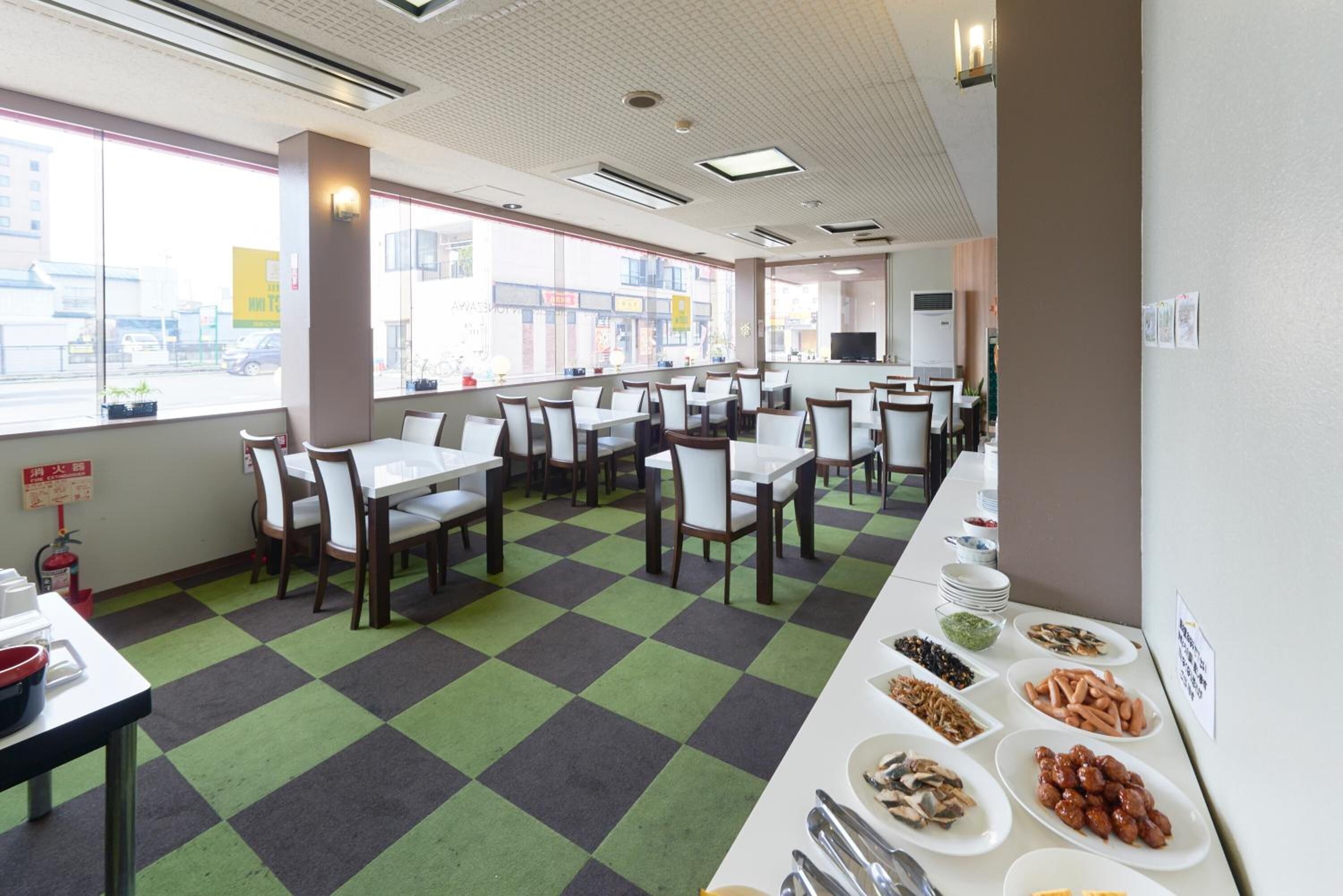 Ein Essbereich mit Tischen und Stühlen, ein Buffet mit verschiedenen Speisen sowie große Fenster mit Blick auf die Straße.