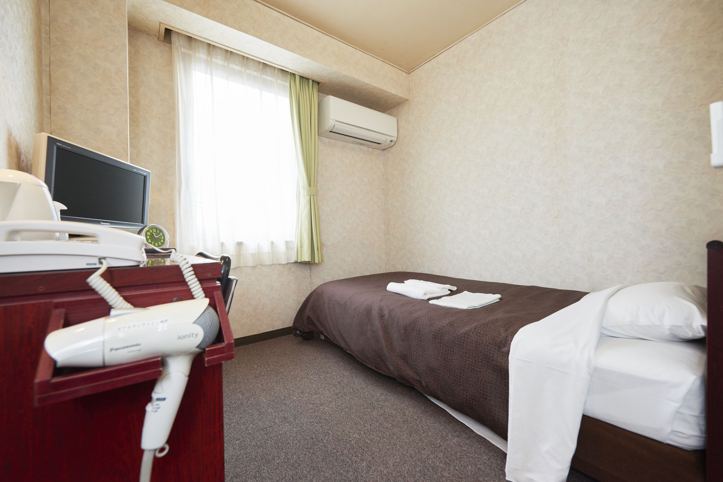 Una camera d'albergo con un letto, una scrivania con asciugacapelli, una televisione e un condizionatore d'aria.