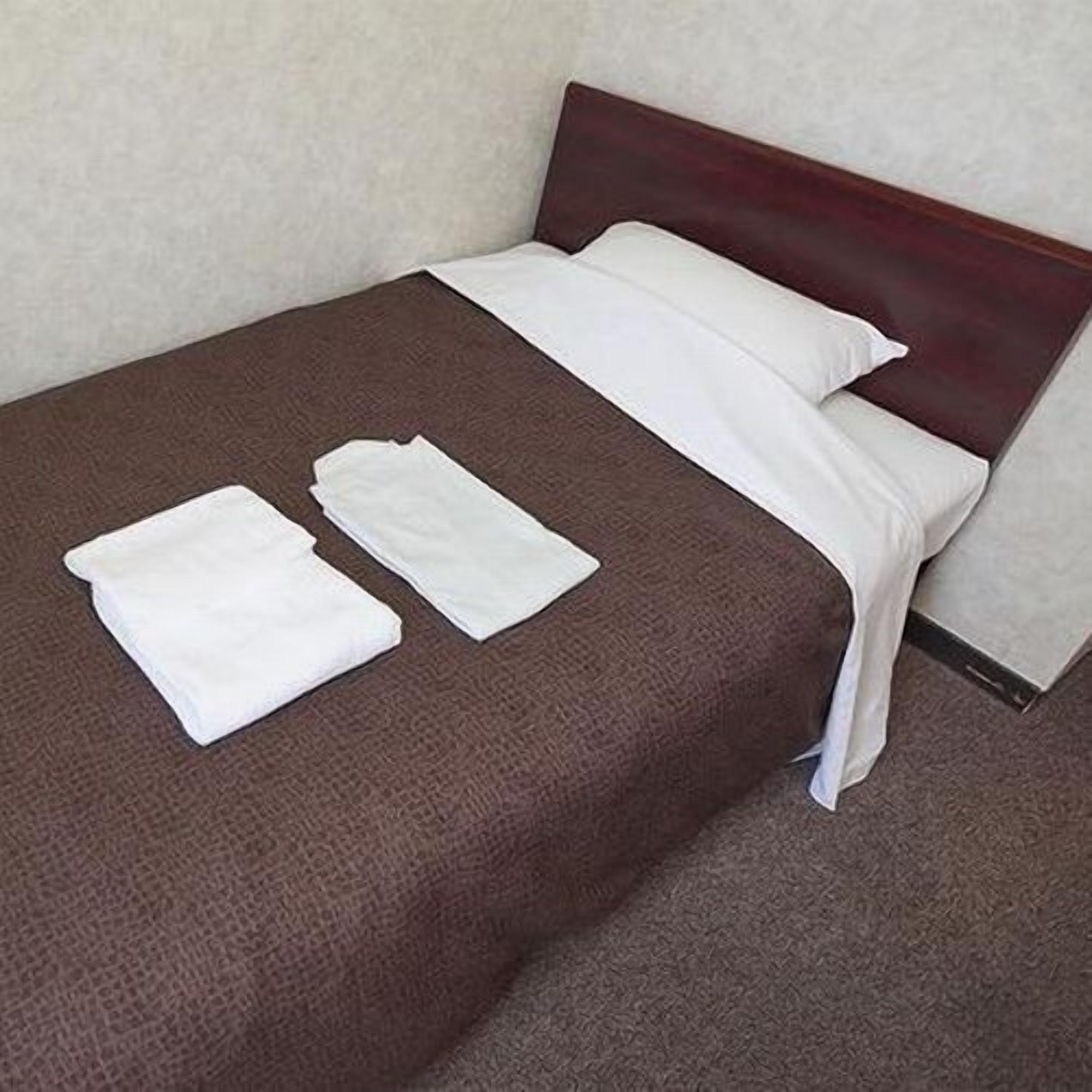 A bed with a brown bedspread, white pillows, and two white towels.