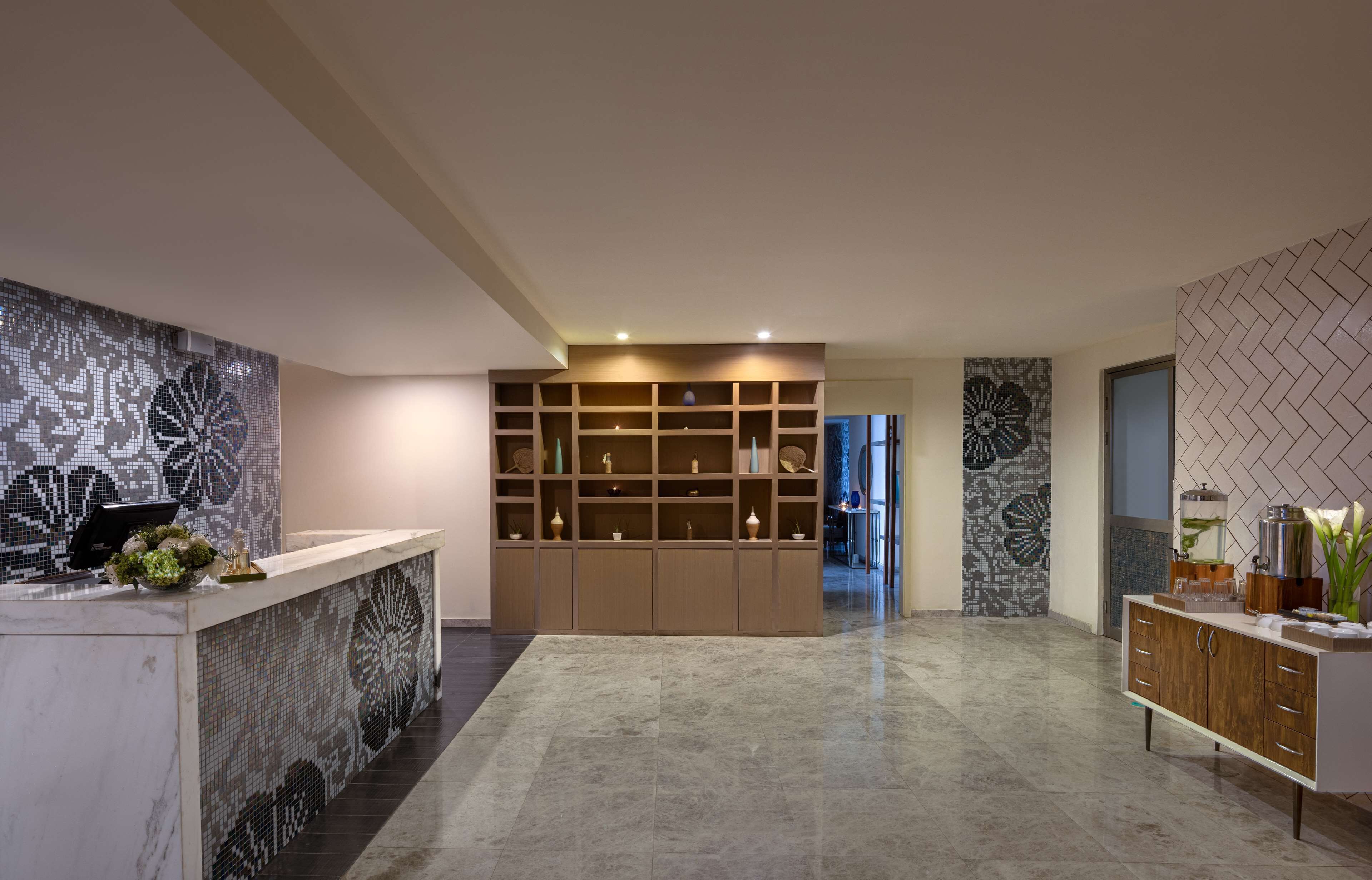 A modern reception area with a marble counter, a mosaic wall, and a central shelving unit with decorative items.