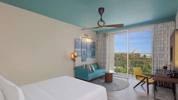 A modern hotel room with a large bed, a sofa, a desk, and a balcony with a view of the city.