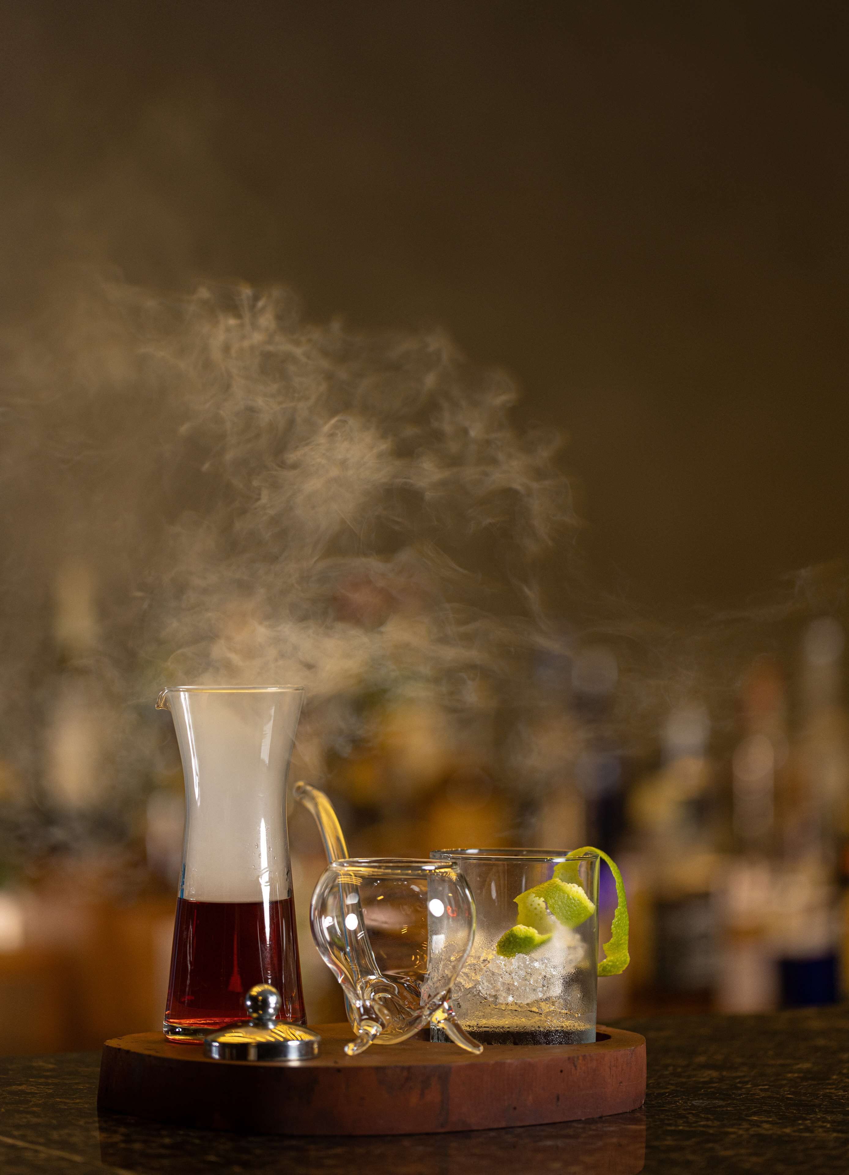A bar setting with a clear glass, a glass of red liquid, and a glass with ice and lime.