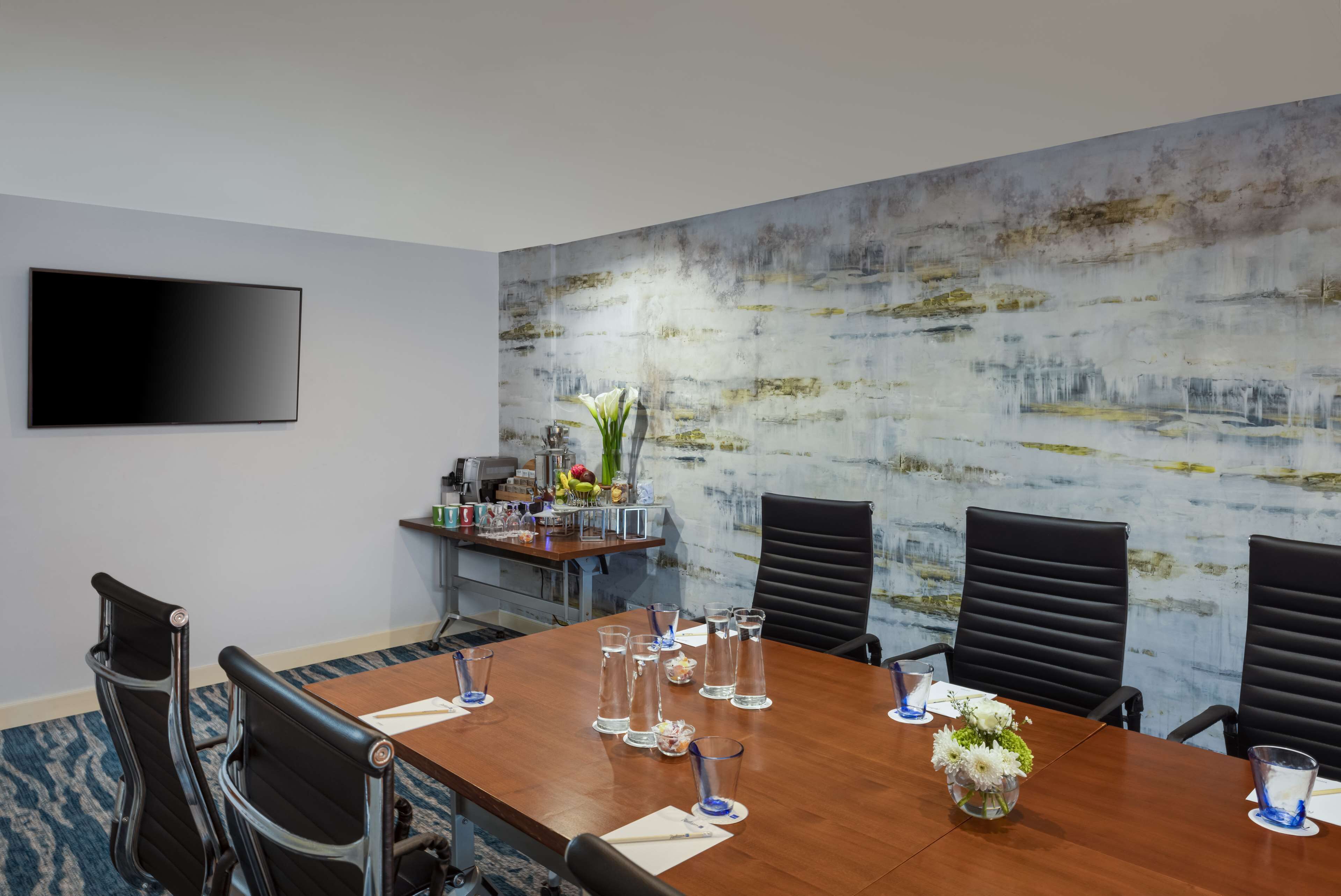 A conference room with a large table, black chairs, and a flat-screen TV mounted on the wall.