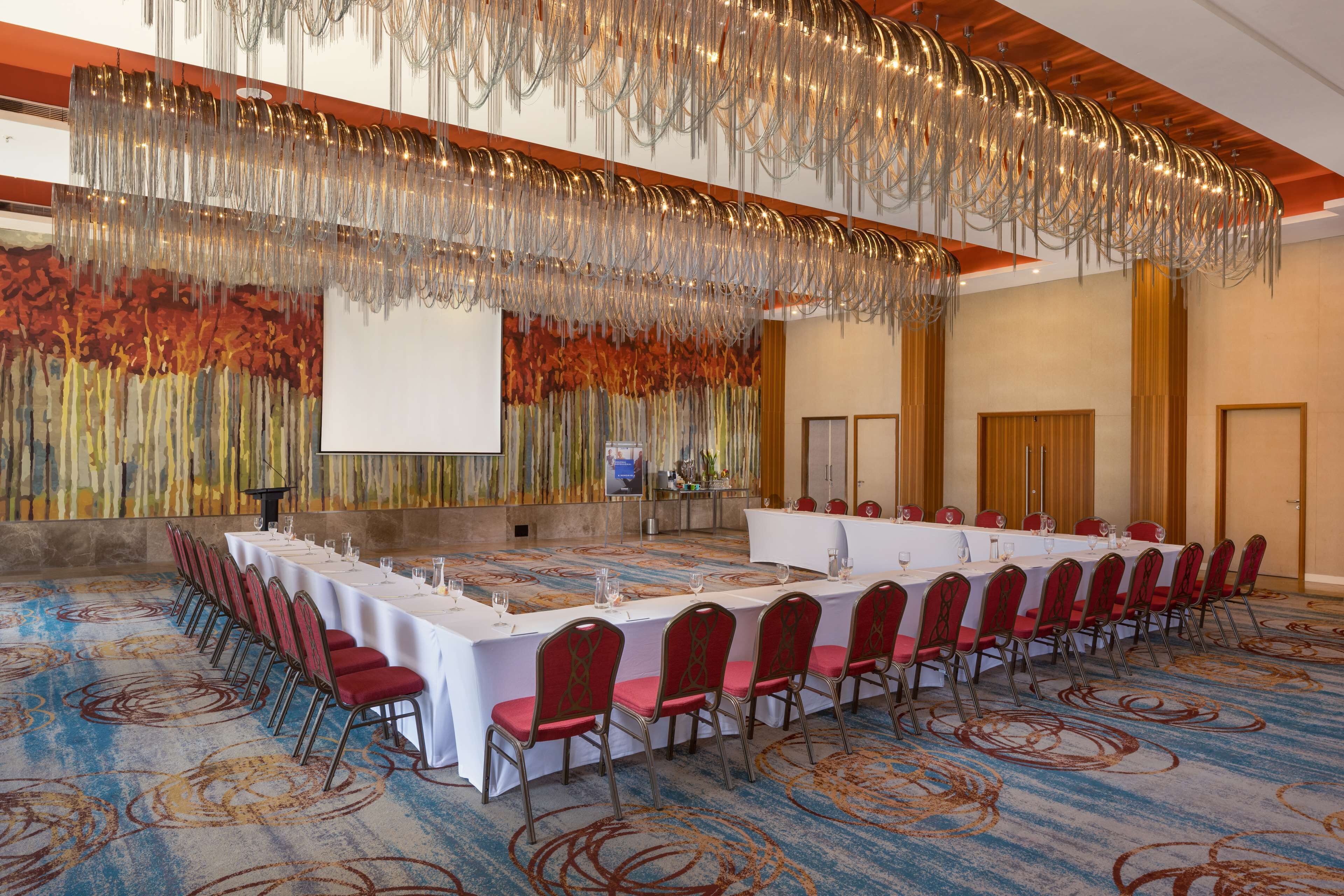 Un salón de conferencias con una mesa larga, sillas rojas y una pantalla grande.