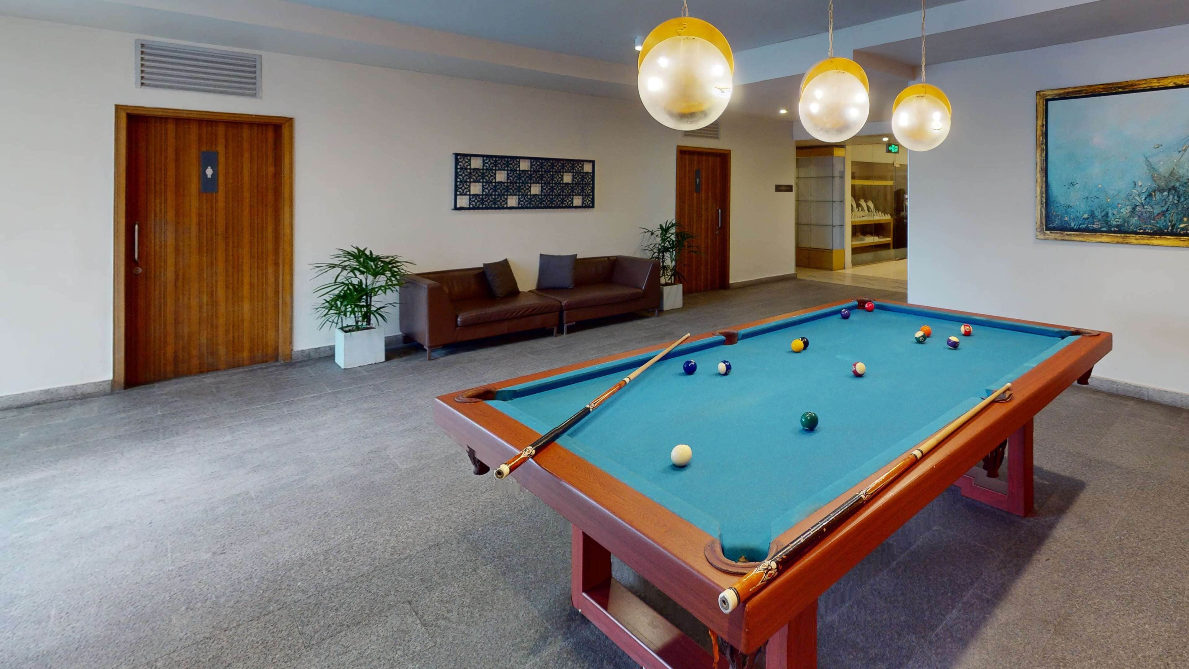 A pool table with balls, a sofa, a potted plant, and a painting on the wall.