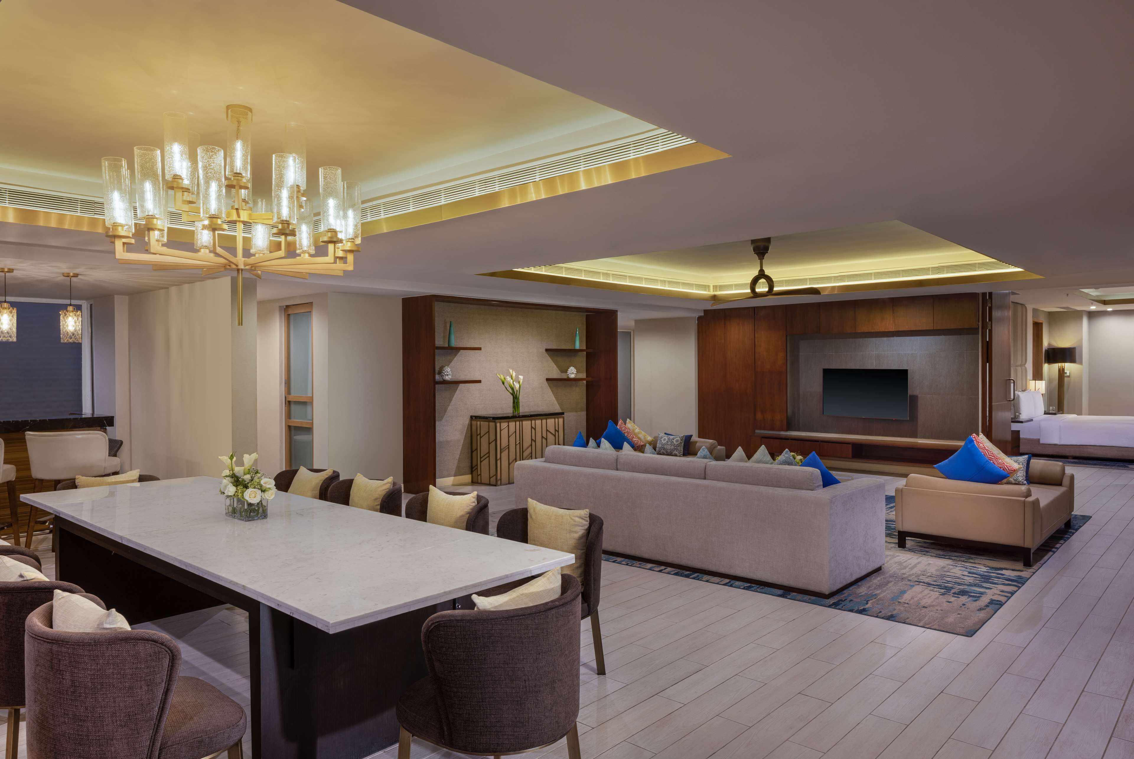 A modern living room with a dining area, a large flat-screen TV, and a chandelier.