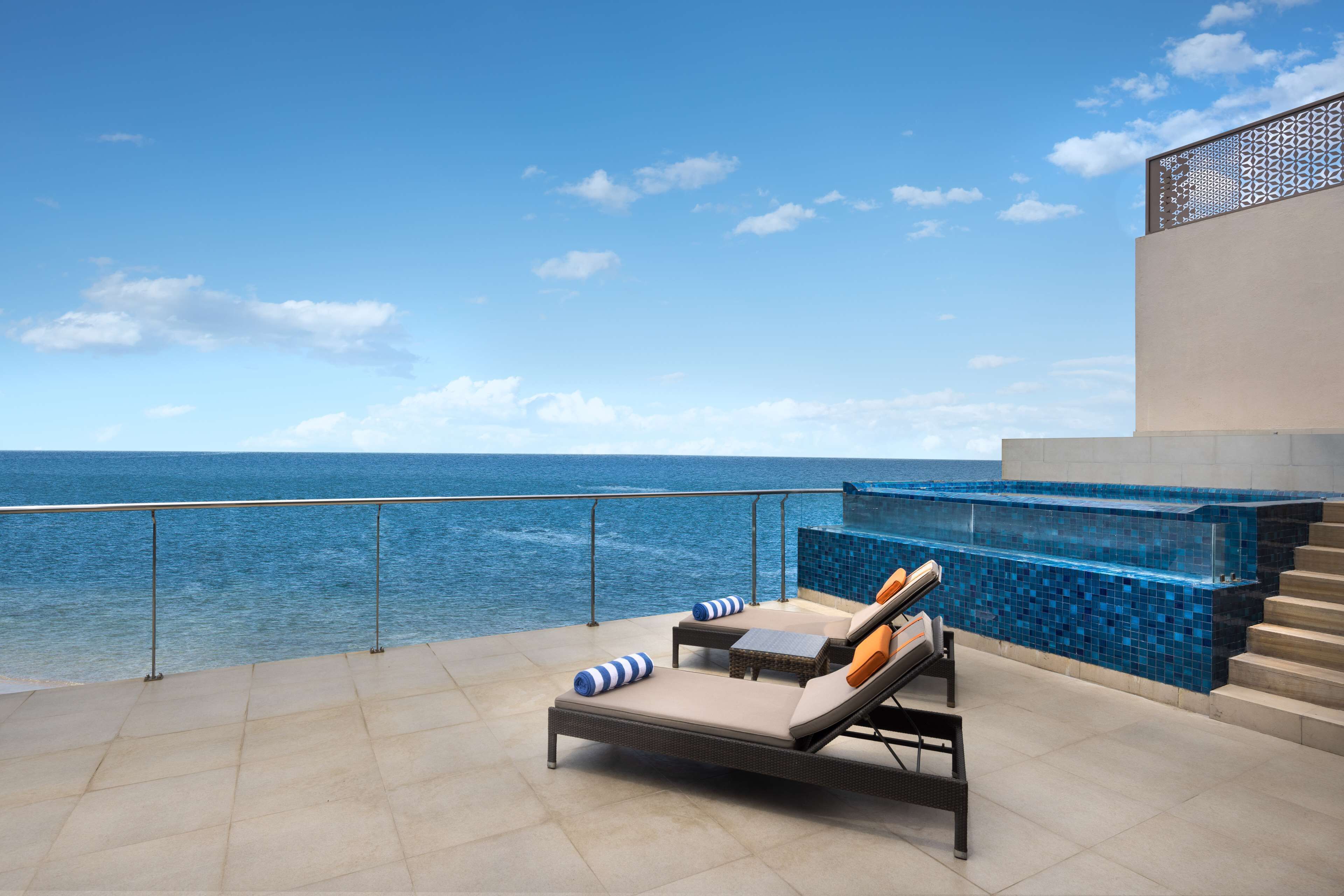 A rooftop terrace with a pool, lounge chairs, and a view of the ocean.