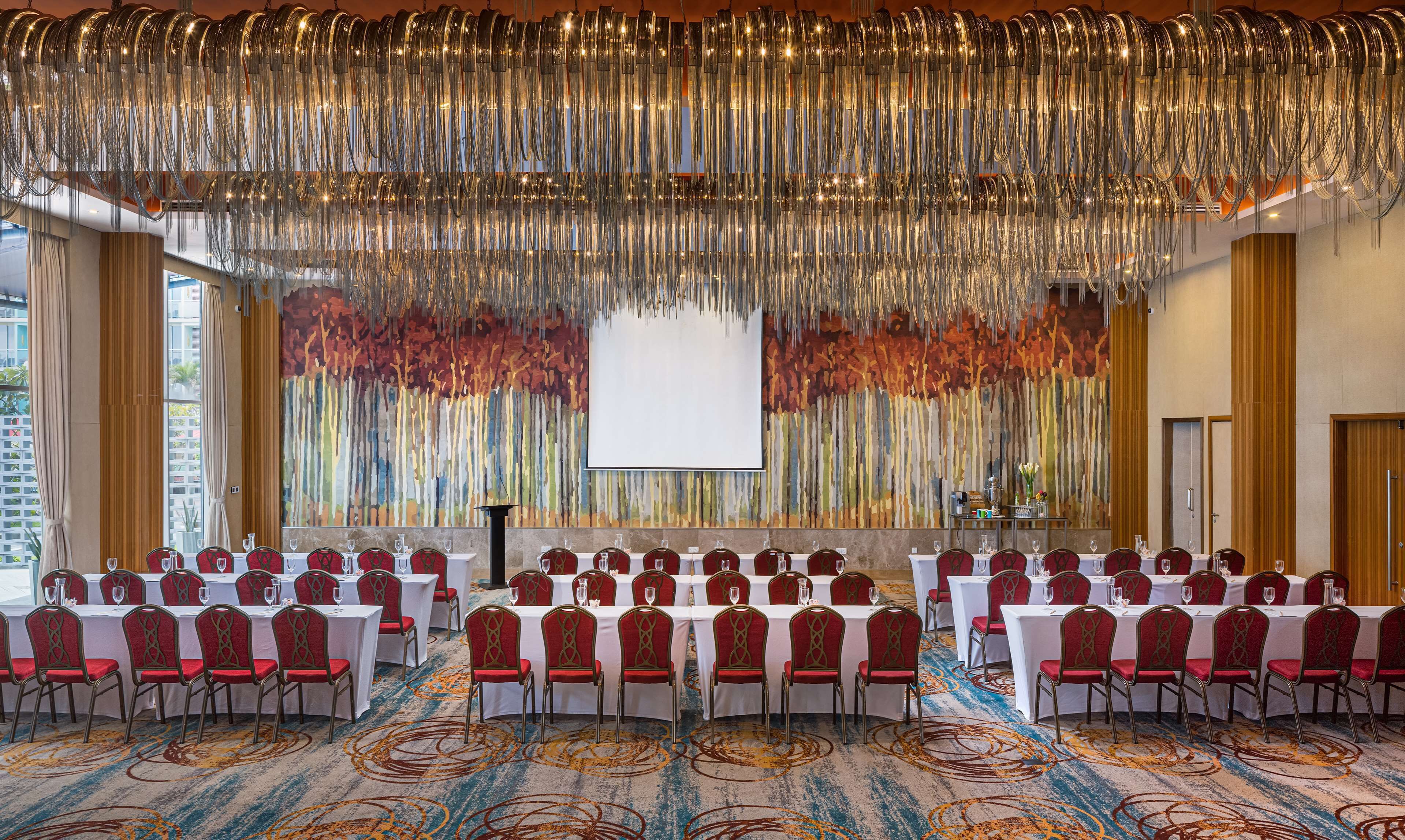 A conference room with rows of tables and chairs, a large screen, and a decorative hanging installation.
