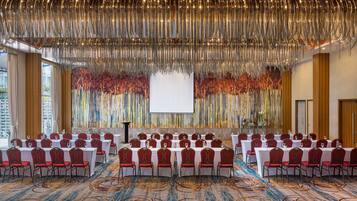 A conference room with rows of tables and chairs, a large screen, and a decorative hanging installation.