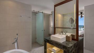 A modern bathroom with a bathtub, a glass-enclosed shower, a large mirror, and a marble countertop with a sink.