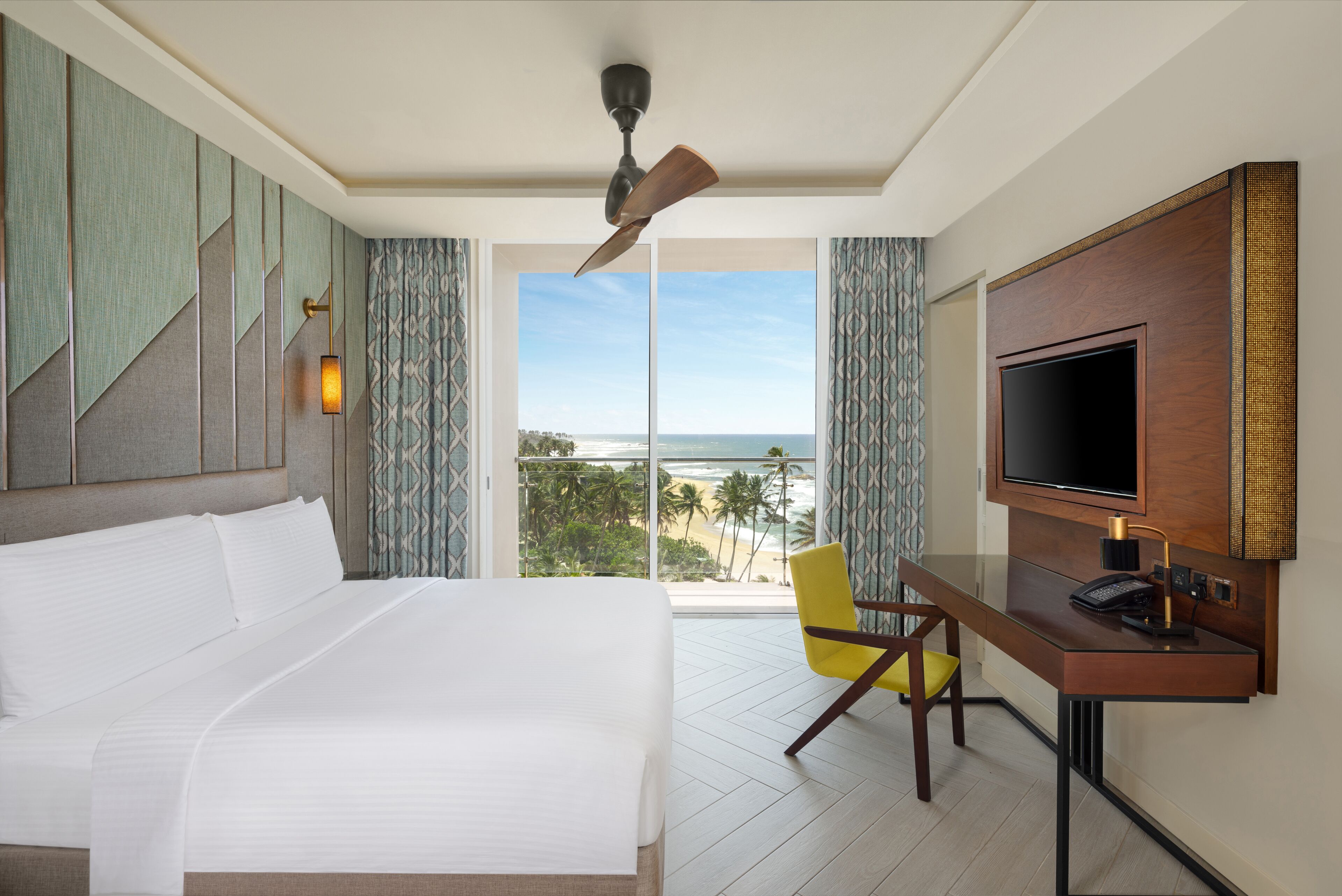 Une chambre d’h ôtel avec un lit, un bureau équipé d’un ordinateur, une télévision et une vue sur la plage.