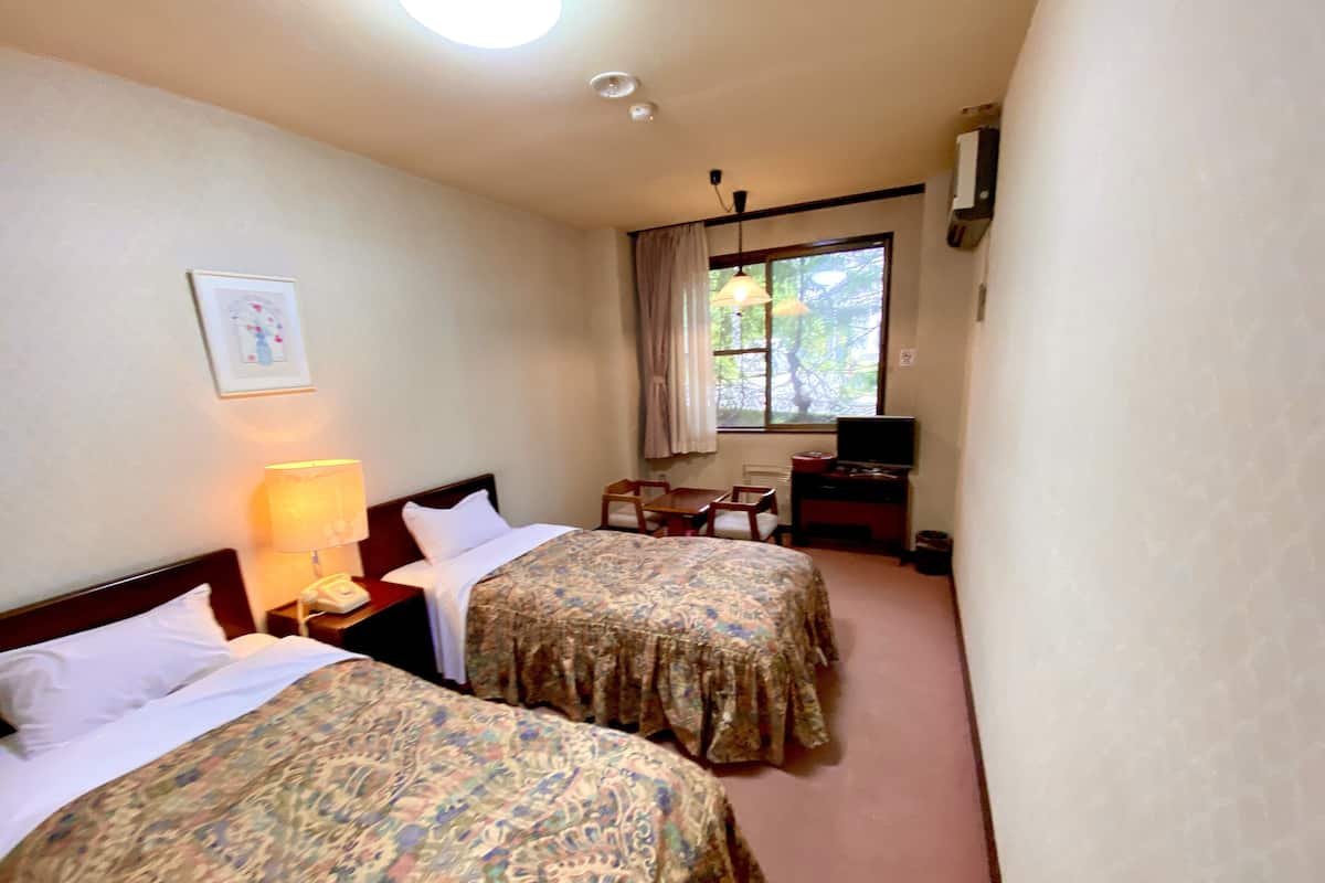 Une chambre d’hôtel avec deux lits, un bureau, une chaise, une télévision et une fenêtre avec des rideaux.