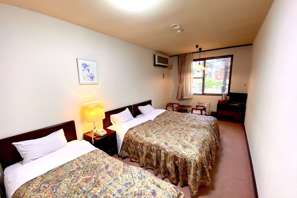 Une chambre d’hôtel avec deux lits, un bureau, une chaise, une télévision et une fenêtre avec des rideaux.