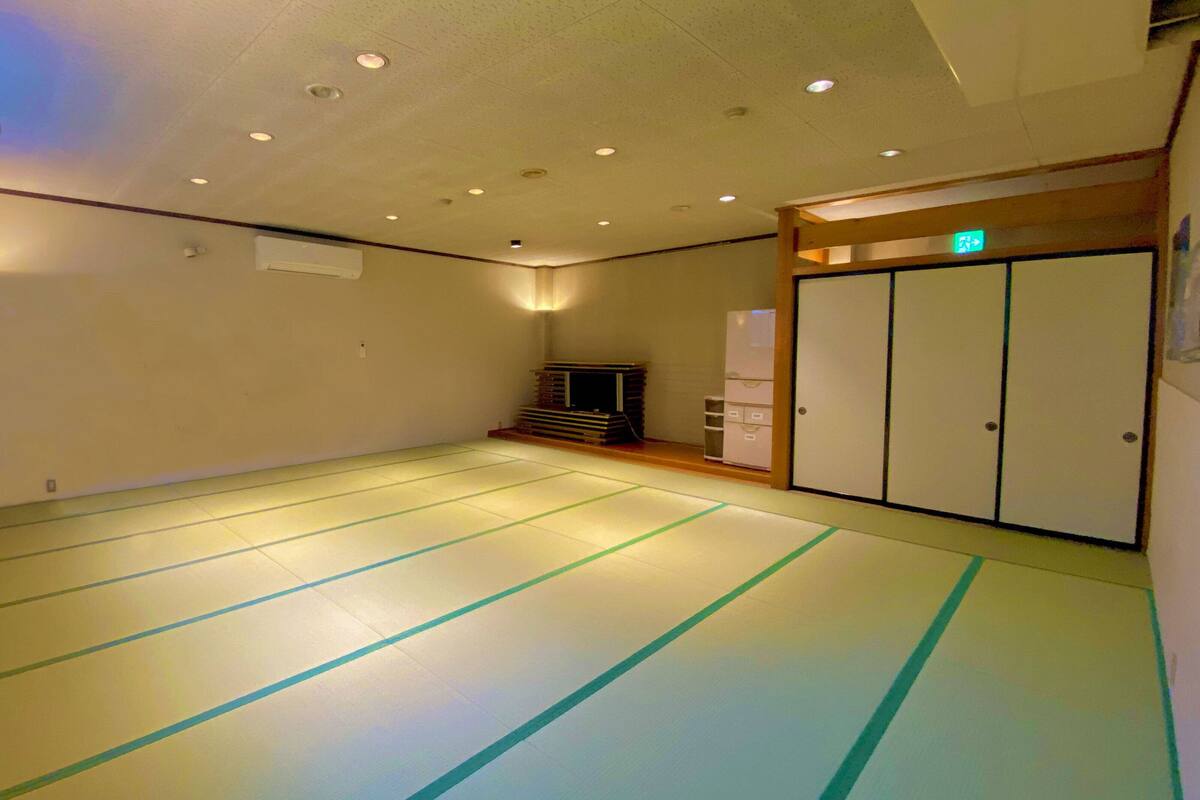 Une pièce avec des tatamis, un aménagement intérieur traditionnel japonais, une porte coulissante et un petit coin salon avec une table basse et des coussins.