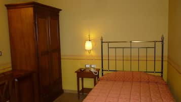 Un dormitorio con cama, un armario de madera, una mesita de noche con lámpara y un aplique de pared.