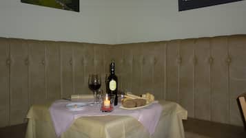 Una mesa de comedor dispuesta con una botella de vino, copas, una vela, pan y un plato de comida.