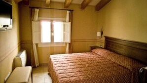 Een slaapkamer met een bed, nachtkastje, stoel, raam met gordijnen en een wandlamp.