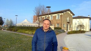 Een man staat voor een gebouw met een bakstenen gevel en een wit dak.