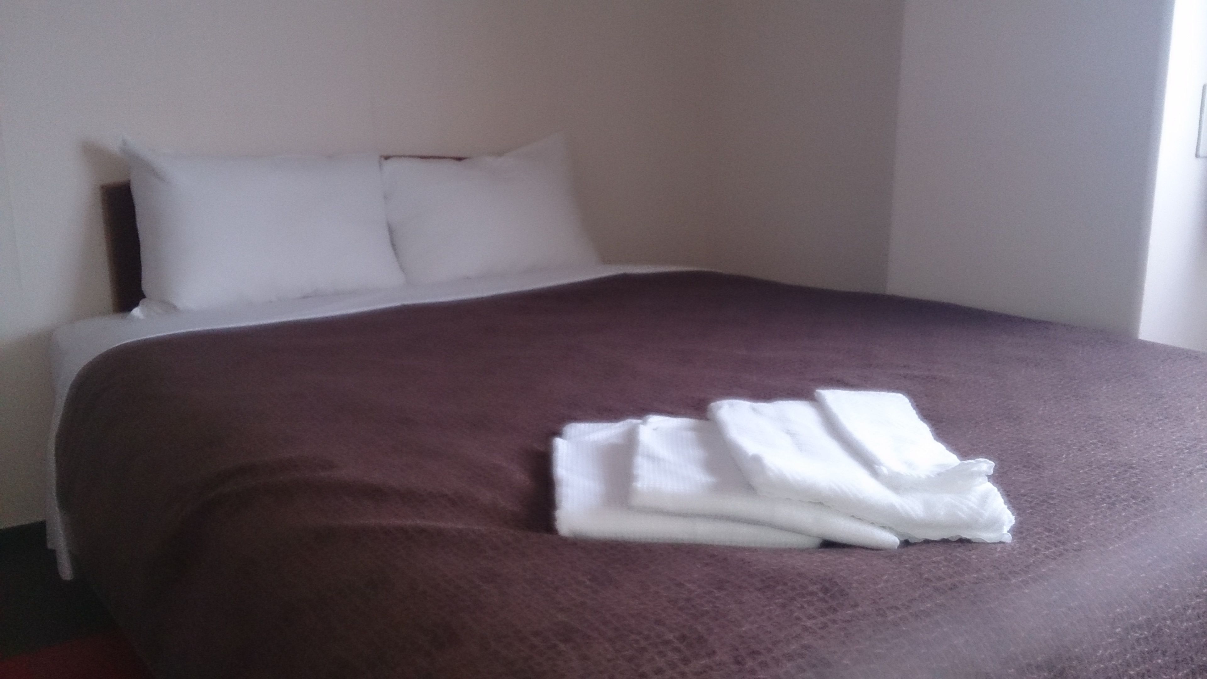A neatly made bed with a brown bedspread and white pillows, and a folded white towel on the bed.