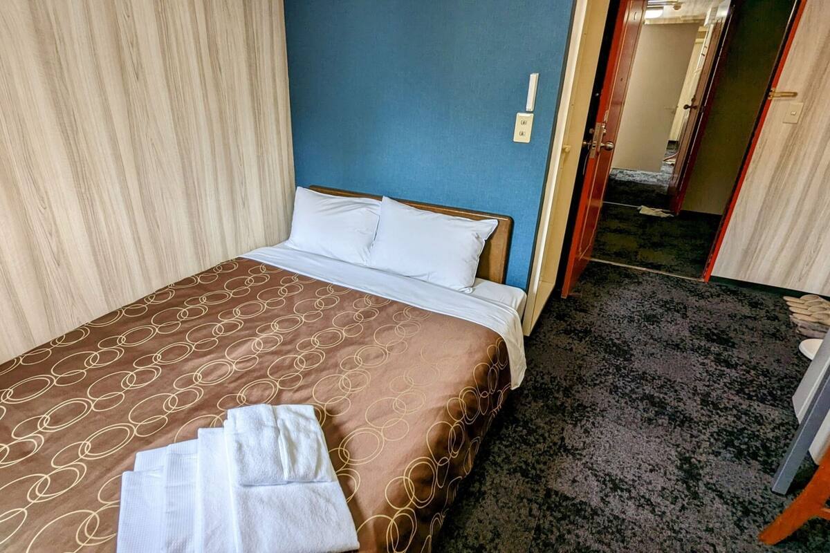 A hotel room with a bed, a blue wall, and a carpeted floor.