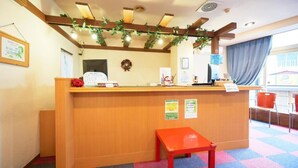 A reception desk with a wooden counter, a red bench, and a check-in counter with a computer and a sign. - Hotel Select Inn Shimada Ekimae (Shimada)