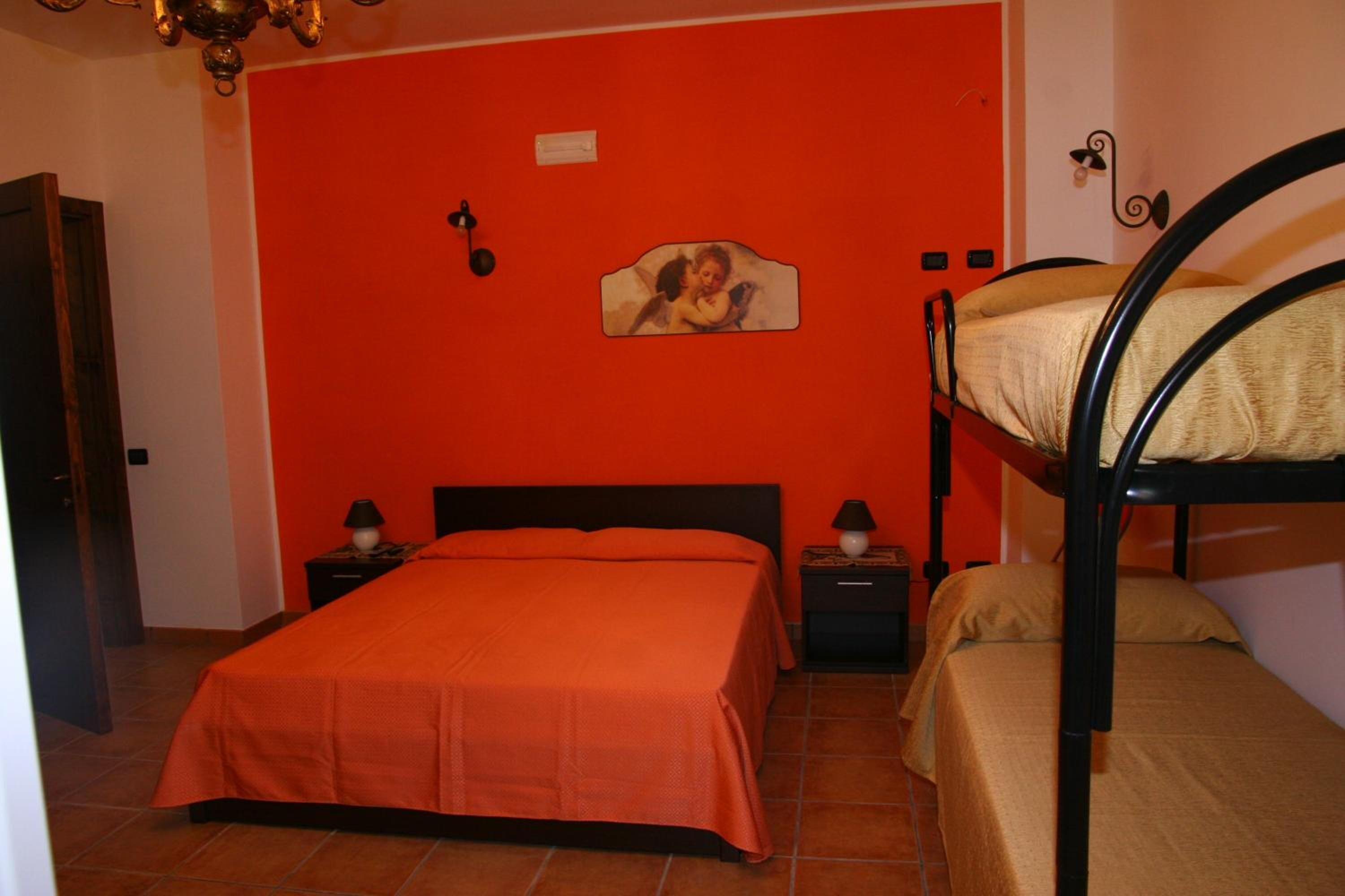 A room with a bunk bed, a single bed, and a red wall.