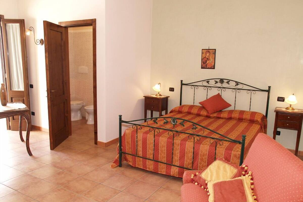 A bedroom with a bed, a nightstand, a dresser, a chair, and a door leading to a bathroom.