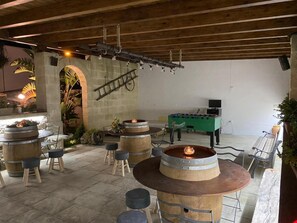 Eine Terrassengaststätte mit Holztischen und -hocker, einem Kicker und einer Feuerstelle.