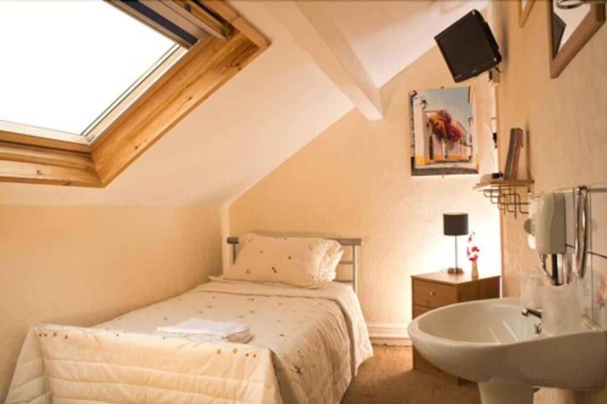 A bedroom with a skylight, a bed, a bedside table with a lamp, and a bathroom with a sink.
