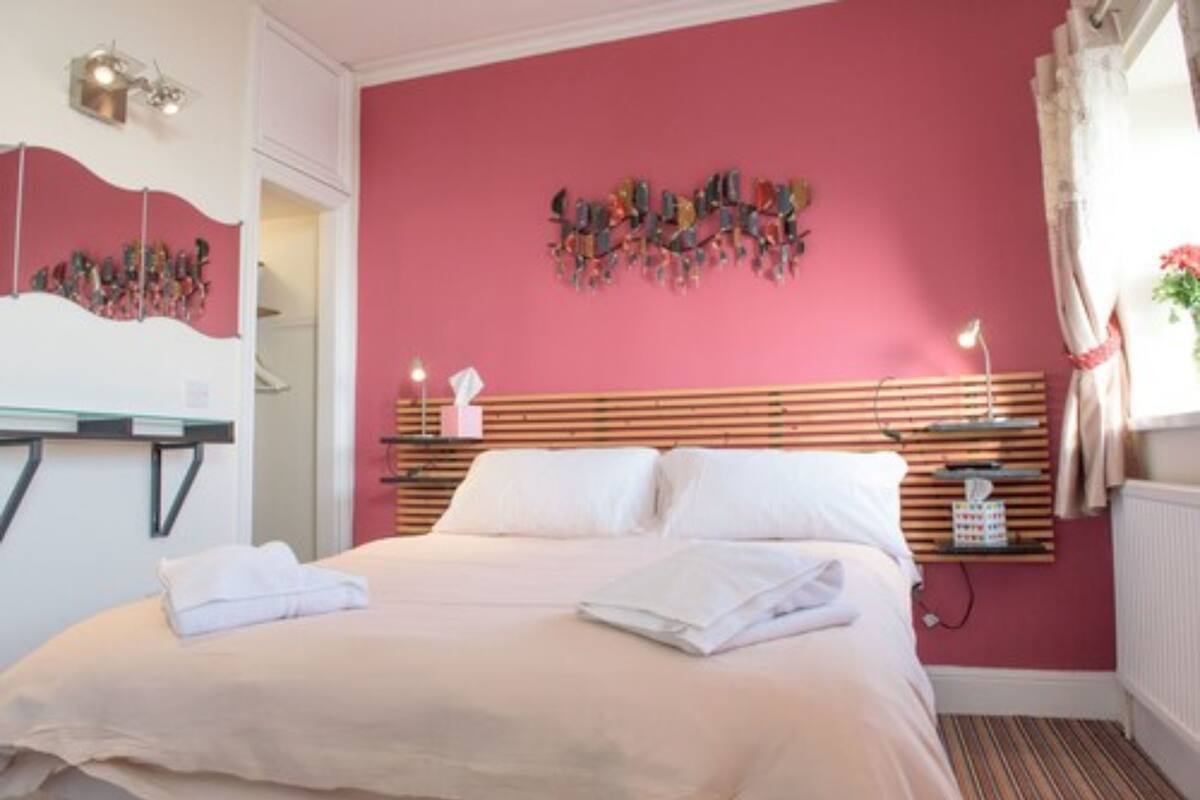 A bedroom with a bed, a bedside table, a wall-mounted artwork, and a window with curtains.