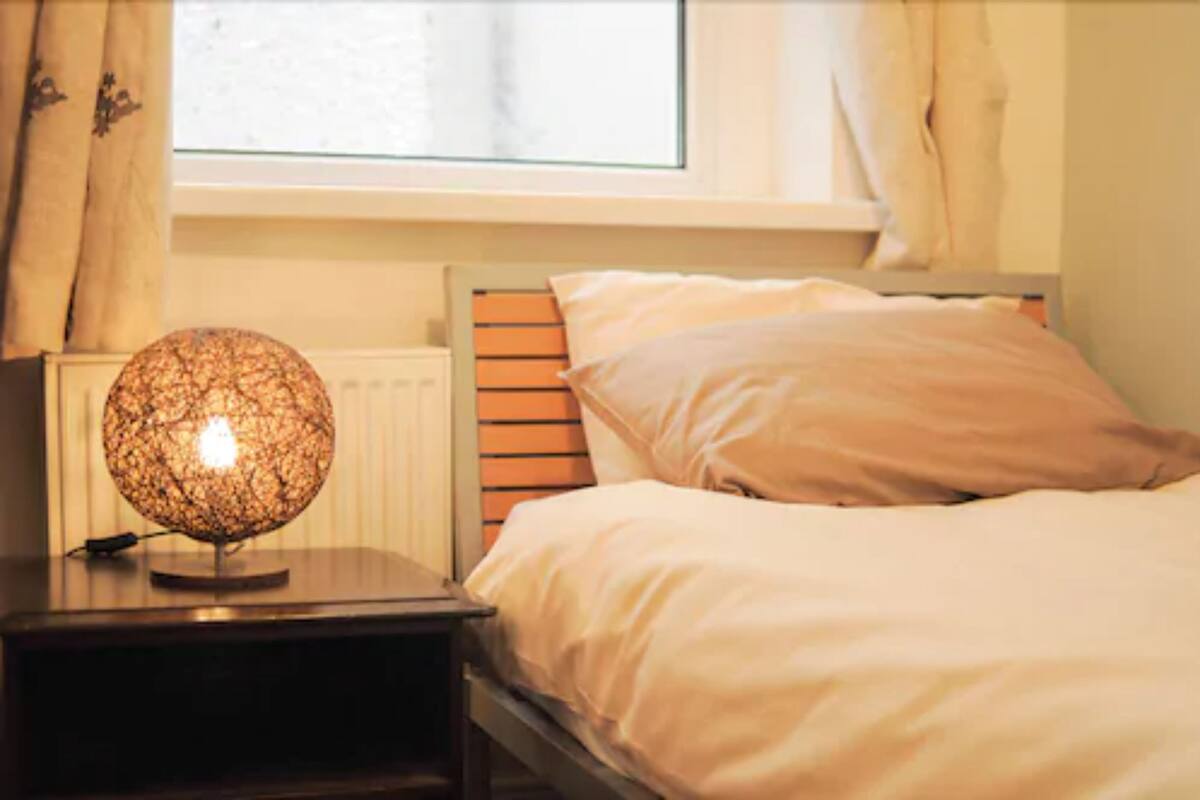 A bedroom with a bed, a bedside lamp, and a window with curtains.