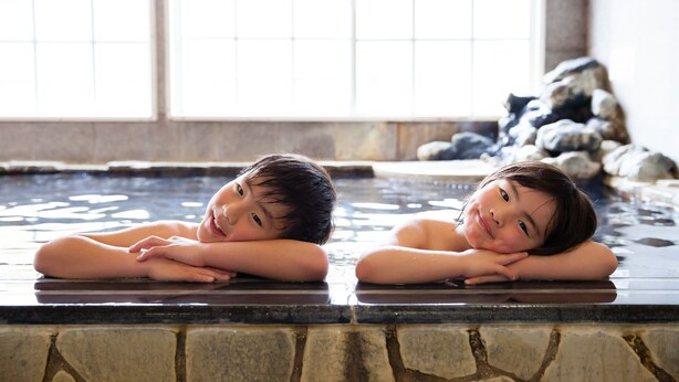 Two children resting in a stone-lined hot spring with a view of rocks and a tiled wall. - Karuizawa Hotel PAIPU NO KEMURI (Karuizawa)