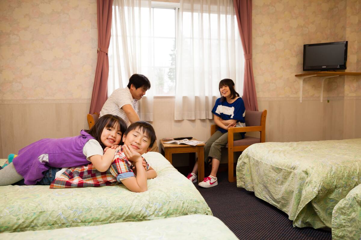 A hotel room with two beds, a television on a stand, and a window with curtains.