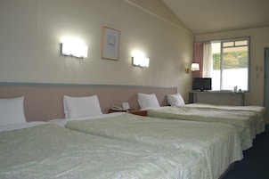 Una habitación de hotel con cuatro camas, un televisor sobre un escritorio y una ventana con cortinas.