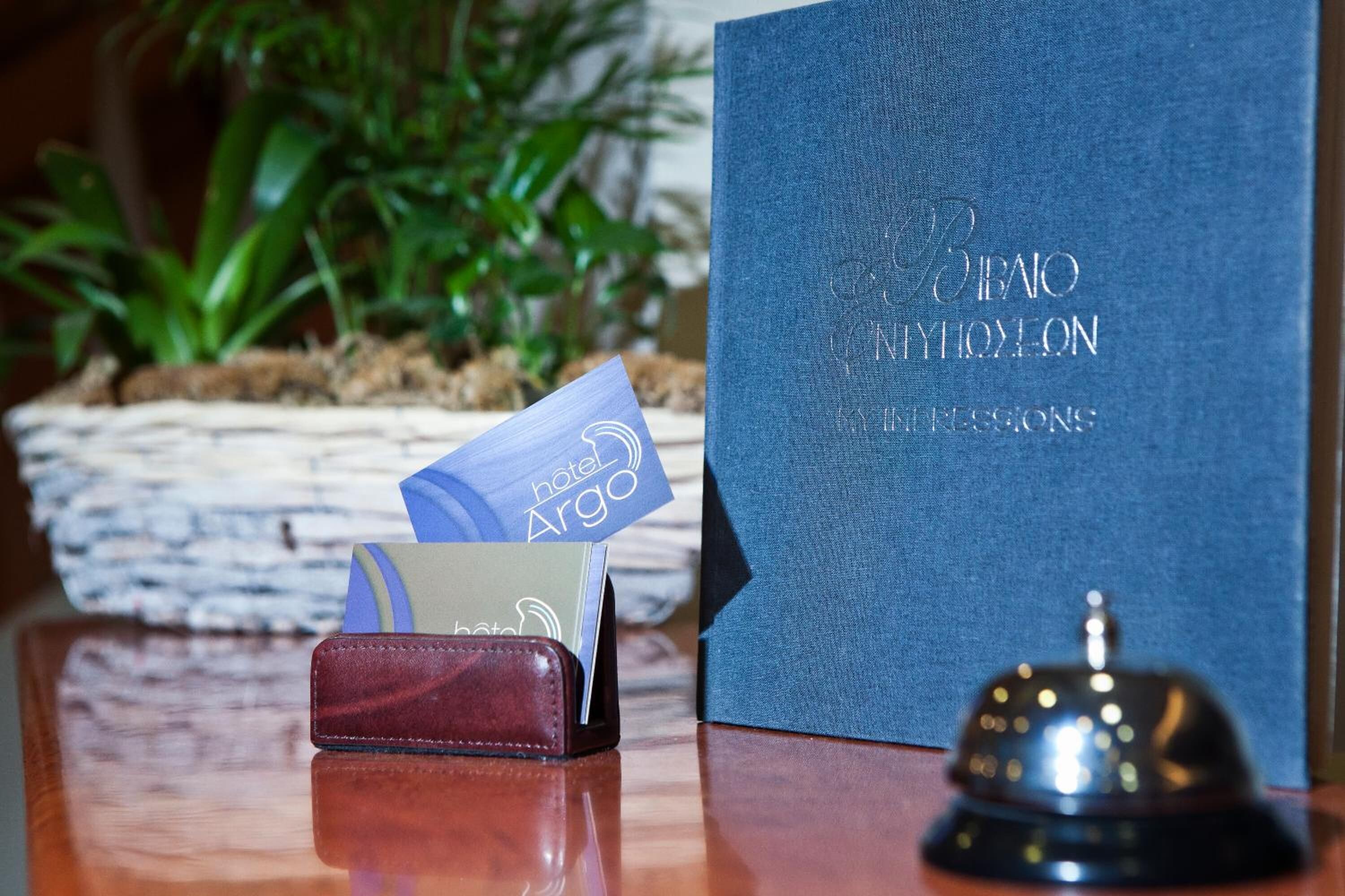 Ein Hotelzimmer mit einem blauen Buch mit dem Titel „Hotel Argo“, einer Brieftasche und einer Glocke auf einem Holztisch.