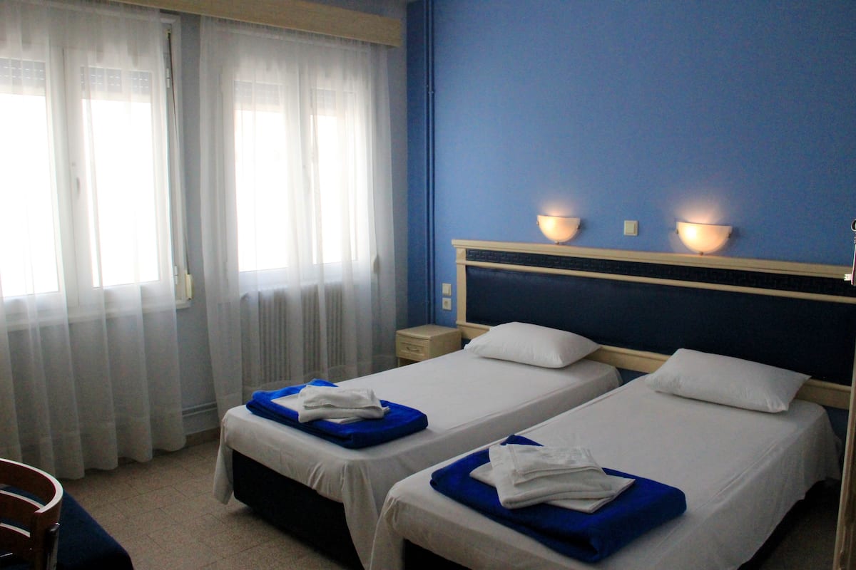 Una habitación de hotel con dos camas, una mesita de noche, una lámpara y una ventana con cortinas.