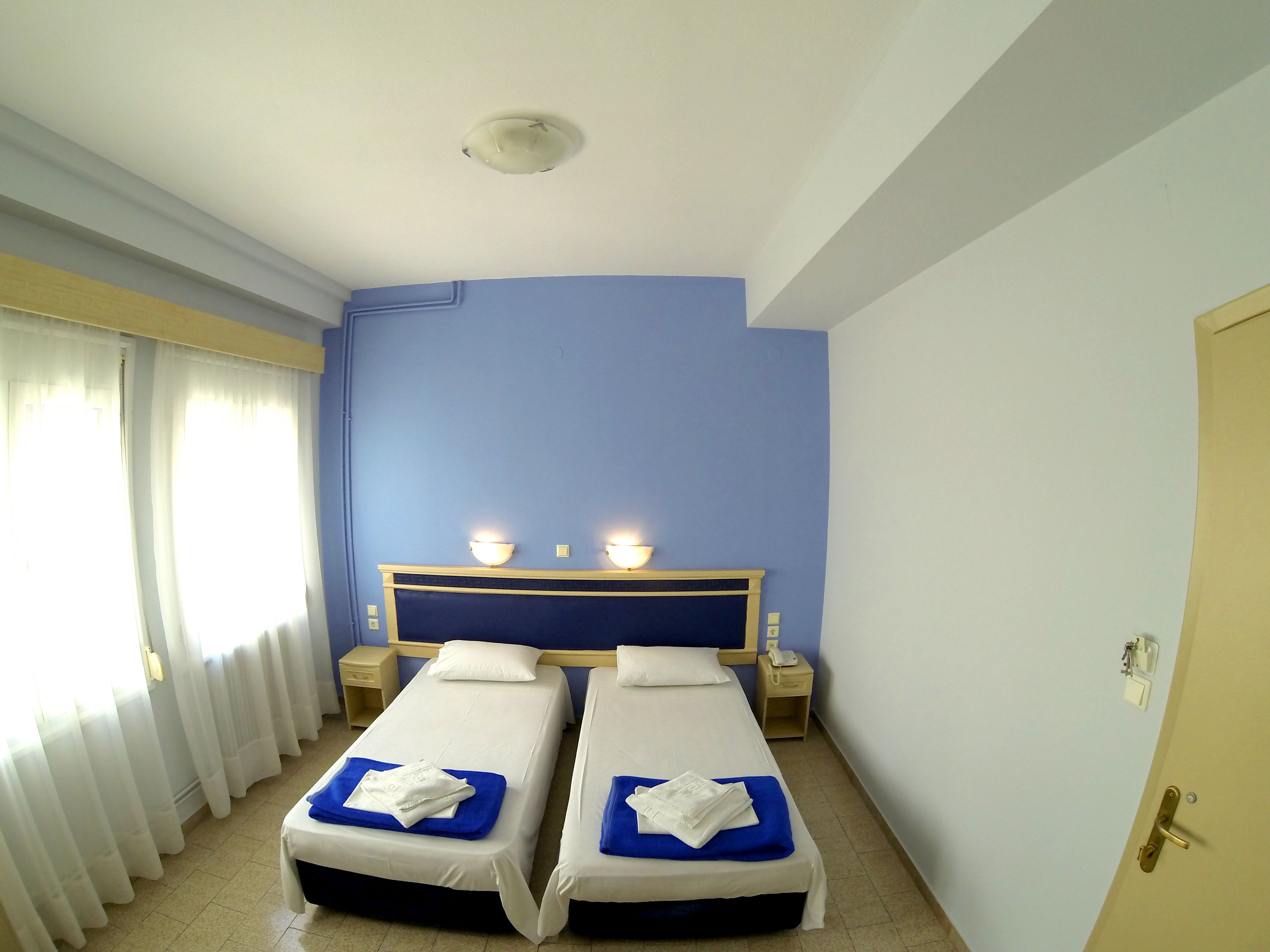 A hotel room with two single beds, a nightstand with a phone, and a window with curtains.