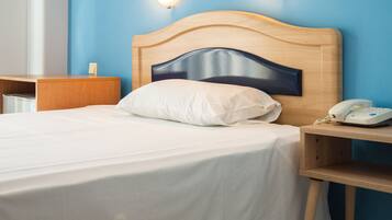 A hotel room with a wooden headboard, a white bedspread, a white pillow, a bedside table with a white telephone, and a wall-mounted light fixture.