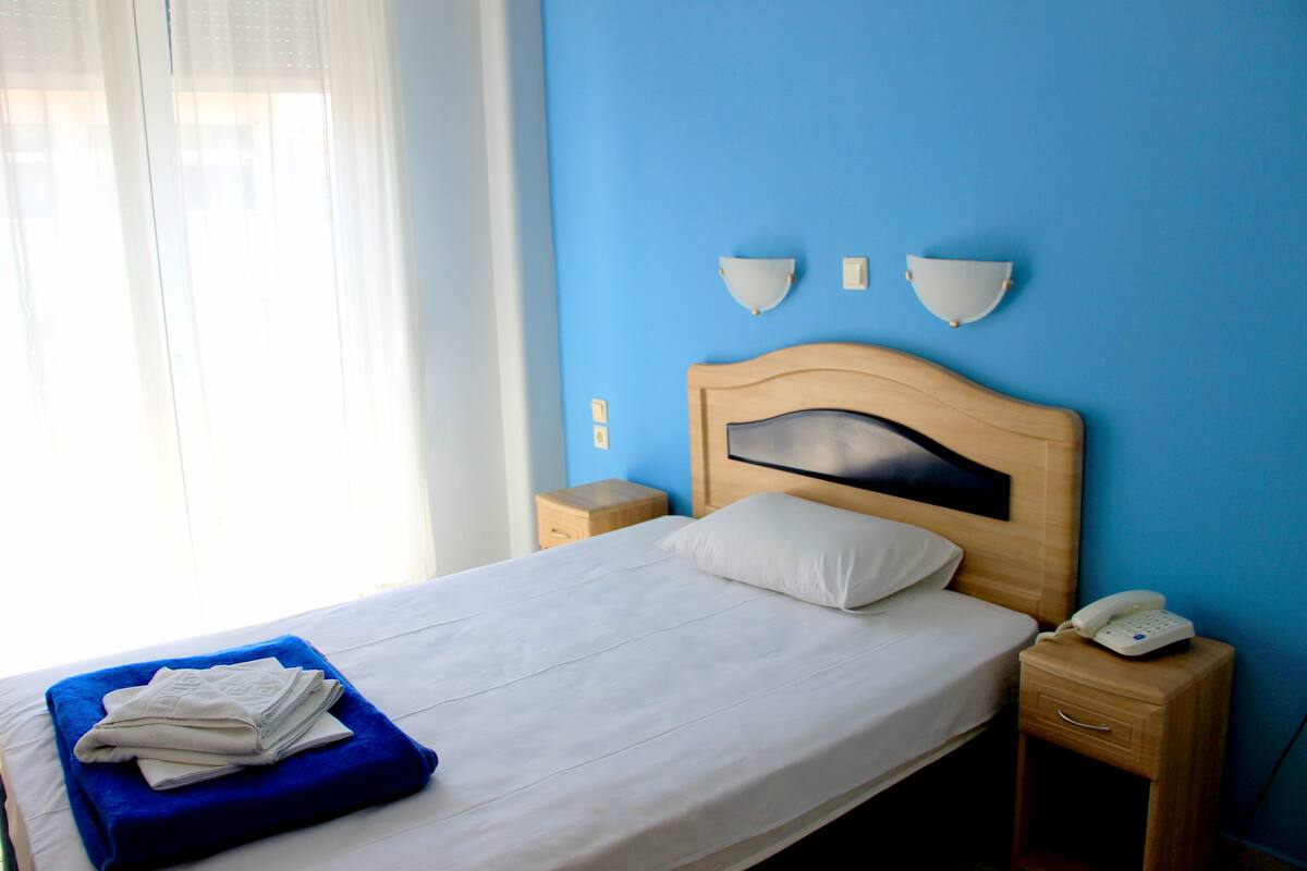 Una habitación de hotel con una cama, una mesita de noche con teléfono, y una lámpara fijada a la pared.