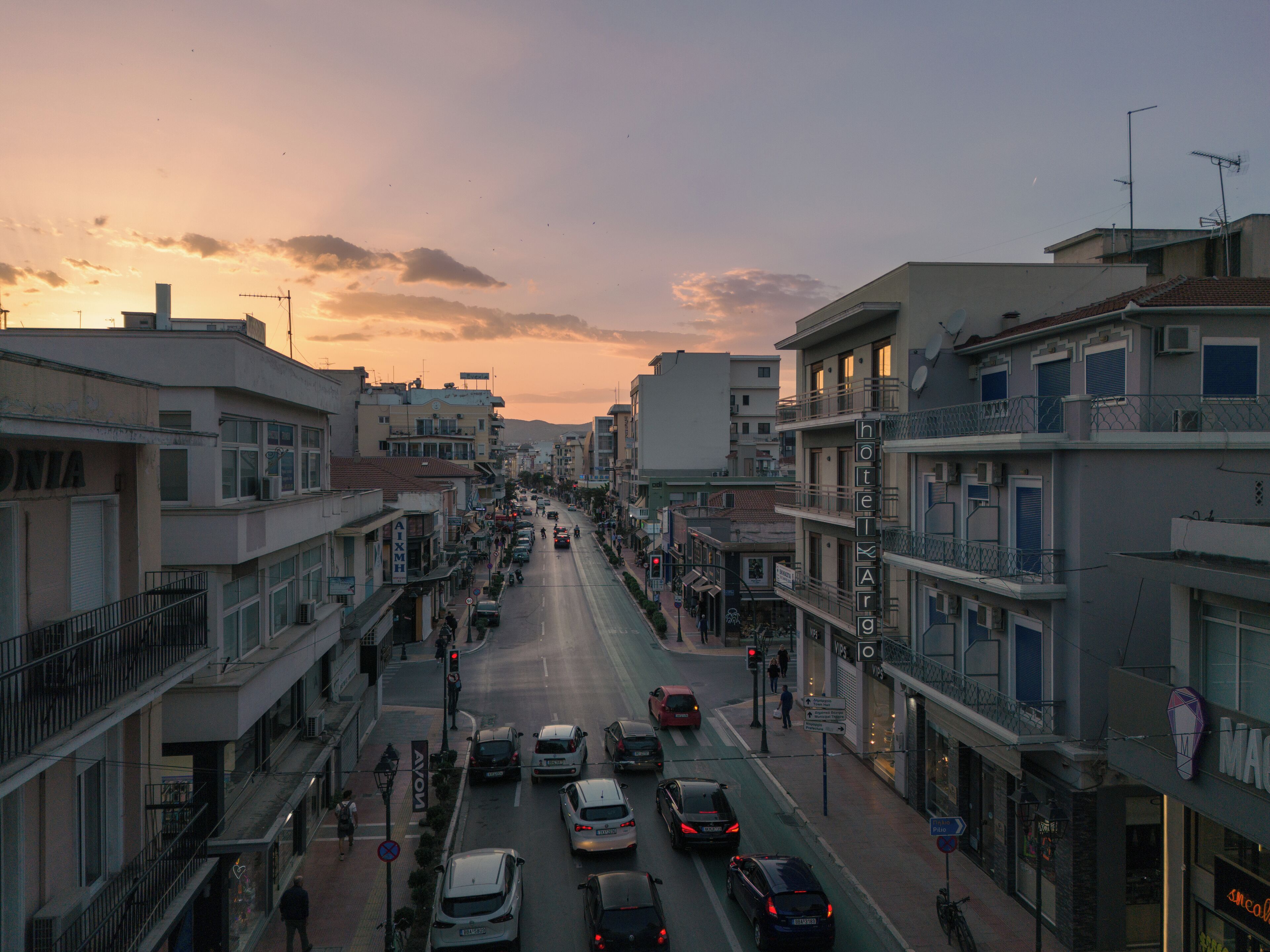 A street view of a city with buildings on both sides, a clear sky, and cars on the road.