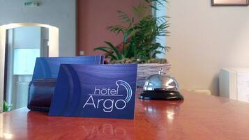 A hotel room with a wooden table, a blue hotel bag, a plant, and a bell.