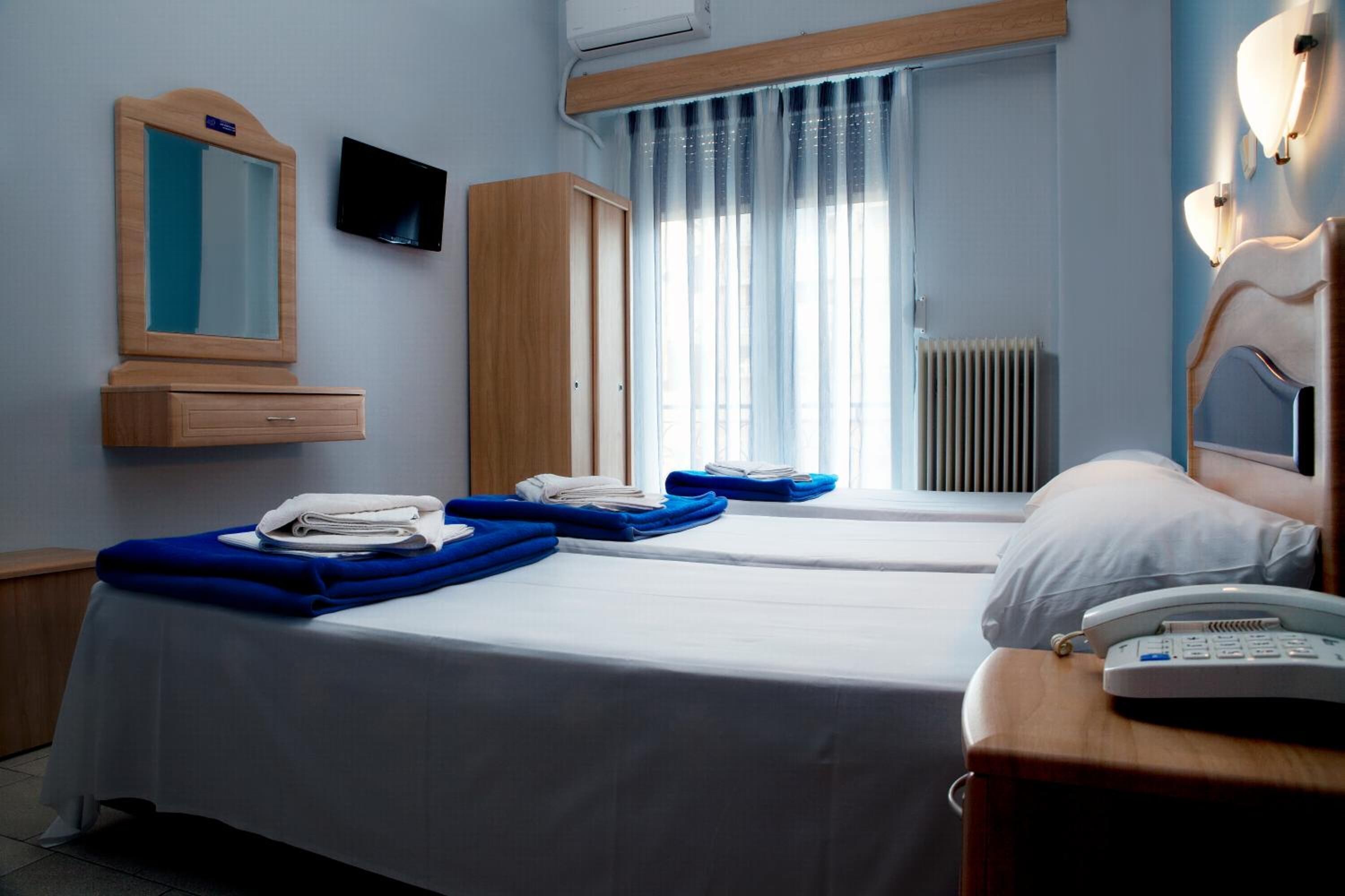 A hotel room with two beds, a wooden wardrobe, a television, a mirror, a radiator, and a bedside telephone.