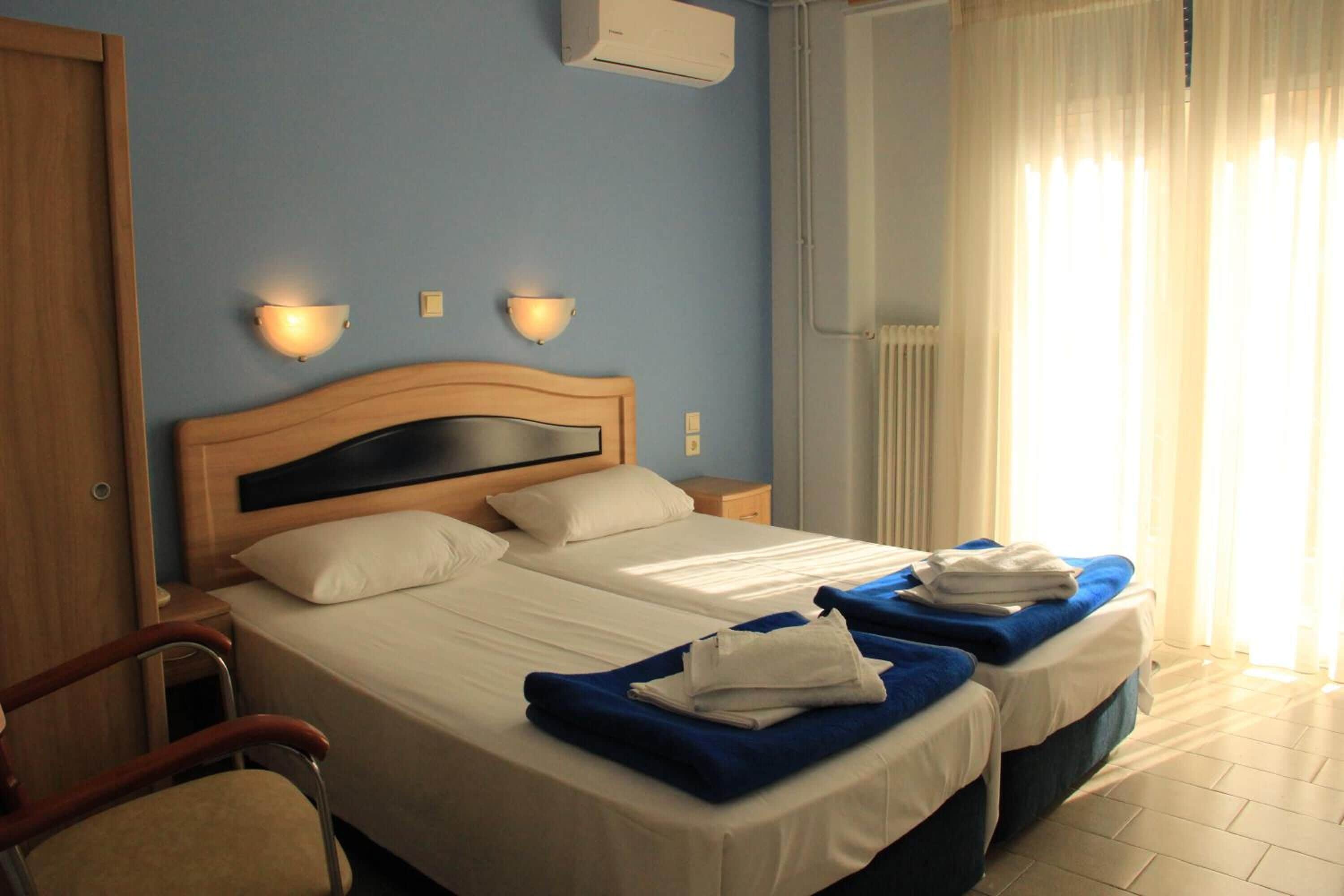 Habitación de hotel con dos camas, cabecero de madera, luces fijadas a la pared y un radiador.