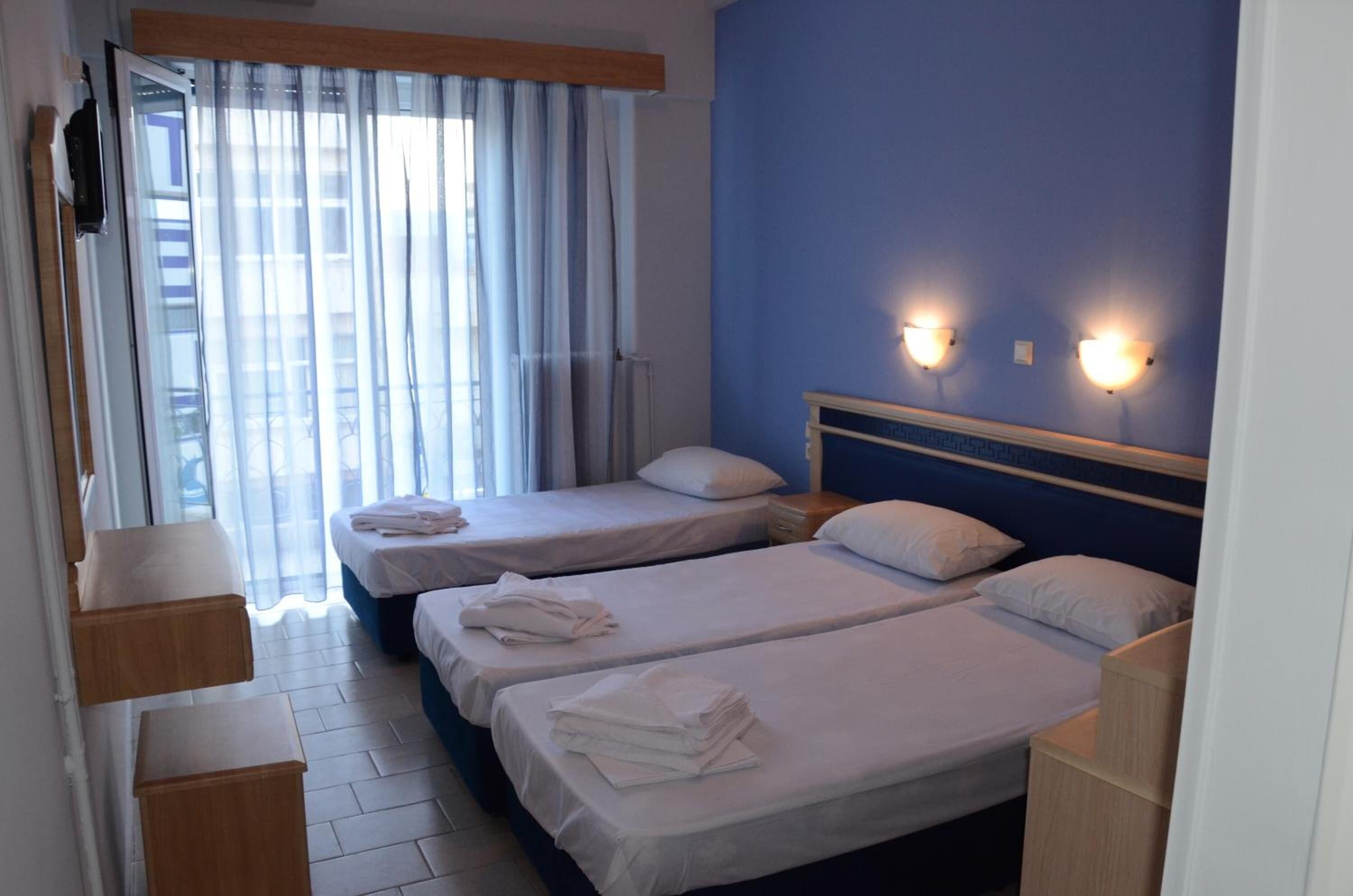 Una habitación de hotel con dos camas individuales, una mesita de noche de madera, una pequeña mesa y una ventana con cortinas.